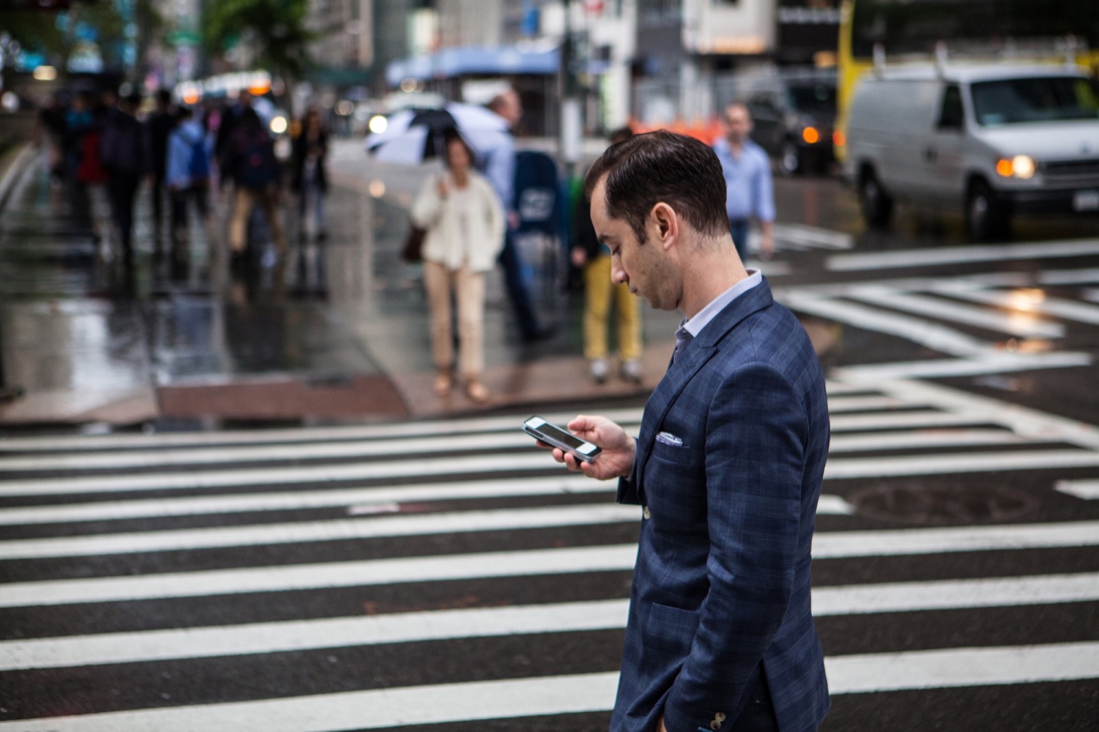 A man in a suit checking his phone as he crosses a street