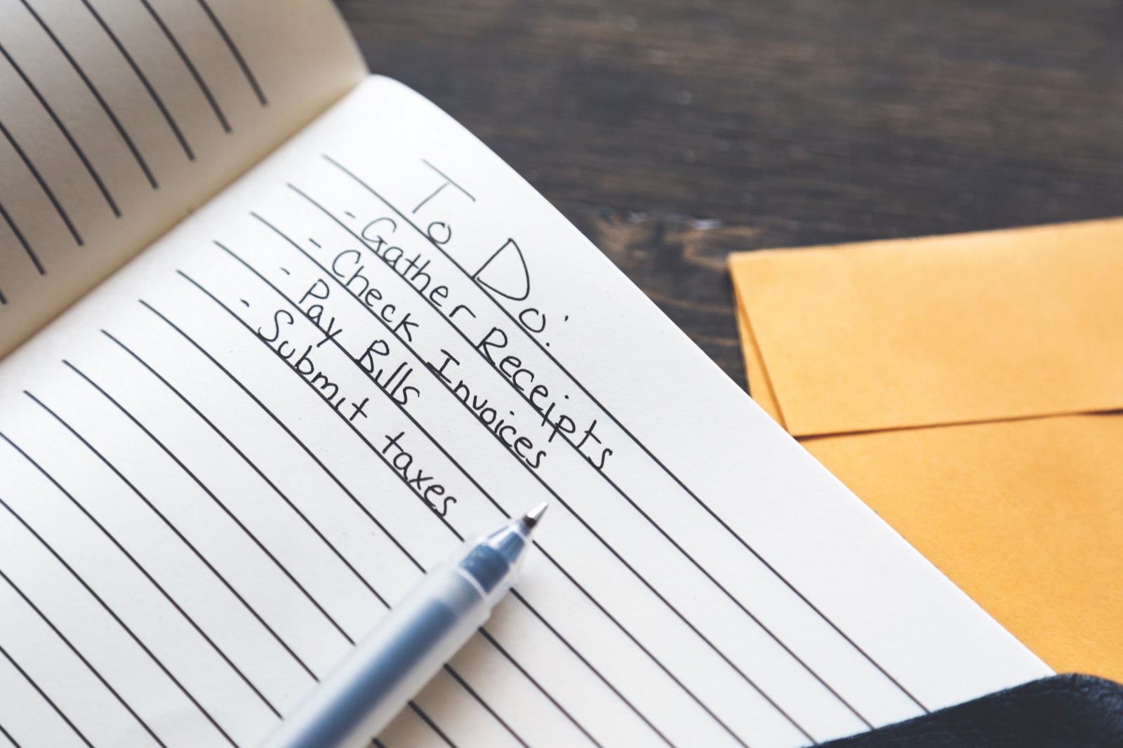 A handwritten to-do list in a notebook beside envelopes